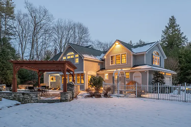House covered in snow with lights on during cloudy winter day.